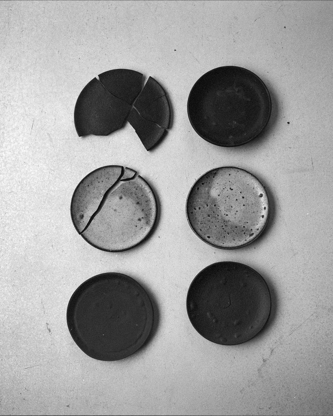 Six small, round plates are arranged in two columns on a light surface, with two of the plates broken.