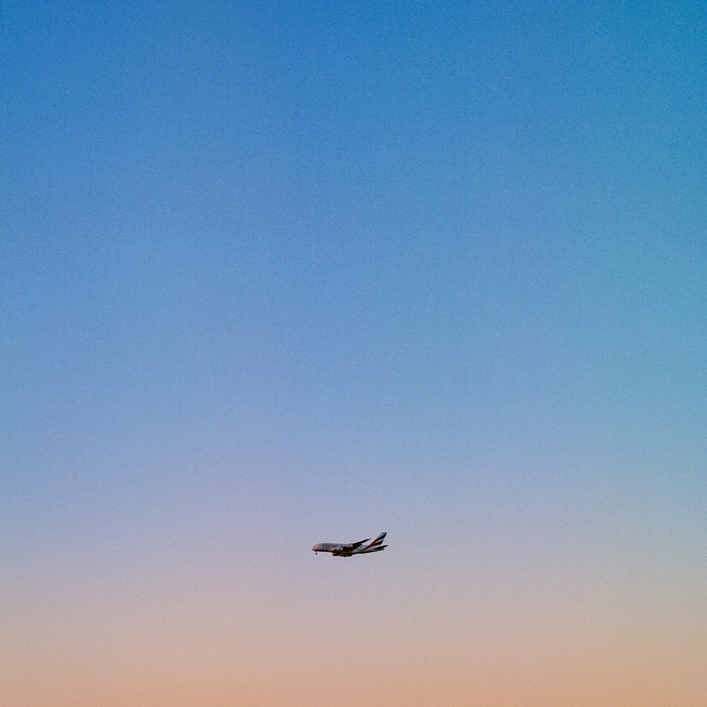 An airplane flies across a gradient sky from blue to orange.