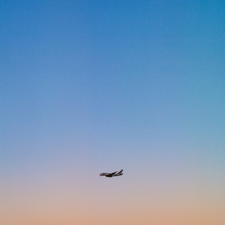 An airplane flies across a gradient sky from blue to orange.