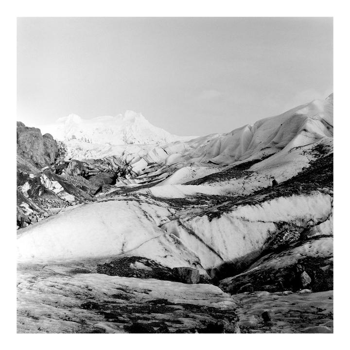 A black and white landscape shows a glacier with snow-covered mountains in the background.