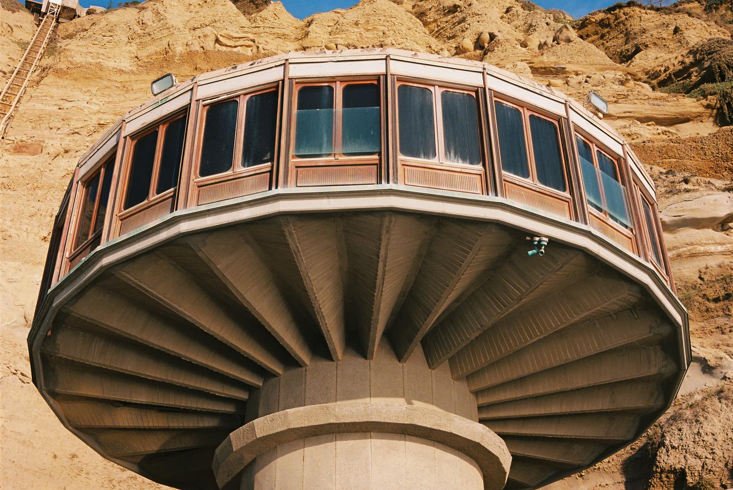 A round building with many windows is built into a sandy cliff.
