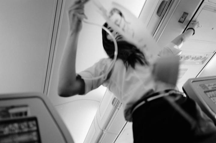 A woman demonstrates an oxygen mask inside an airplane cabin.