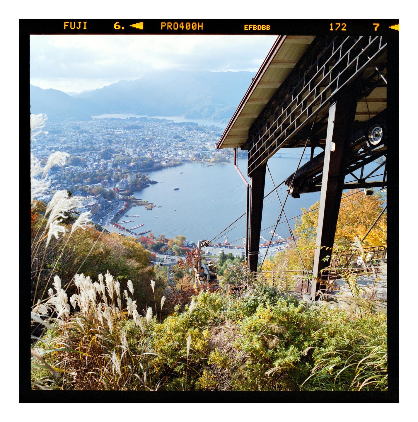 A scenic overview of a town and lake from a high vantage point, with a cable car station in the foreground.