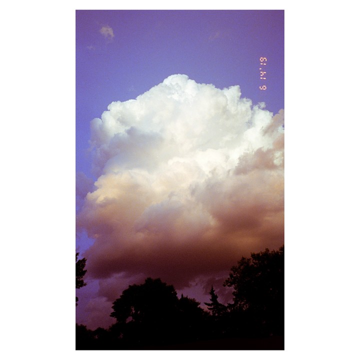 A large cloud formation with dark undersides is visible against a purple sky above silhouetted treetops.