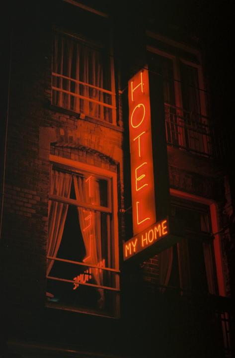A neon sign for a hotel that reads "HOTEL MY HOME" hangs on the side of a brick building at night.
