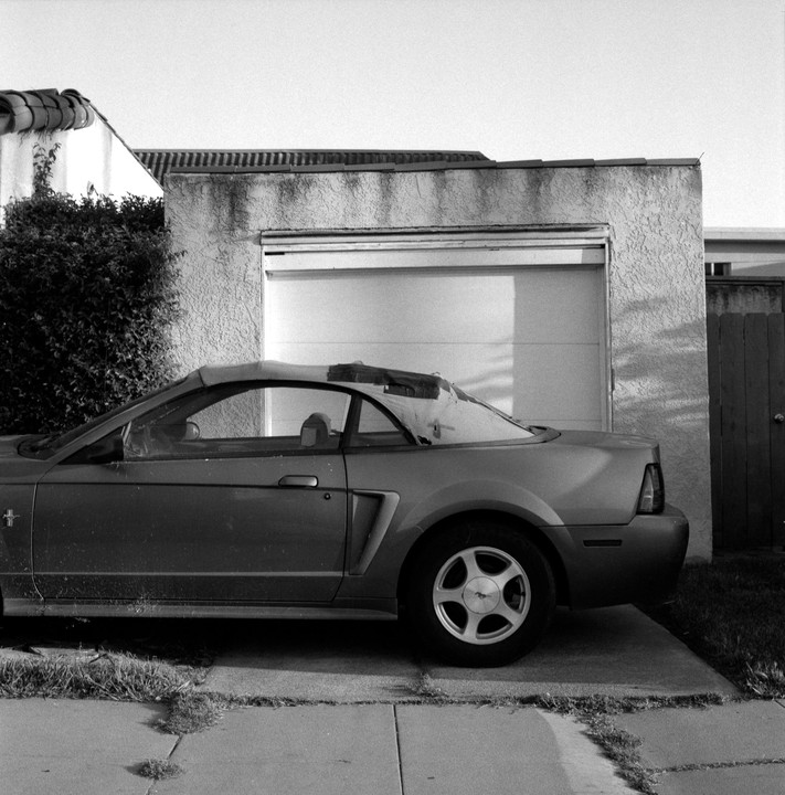 A convertible car is parked on a concrete driveway next to a garage.