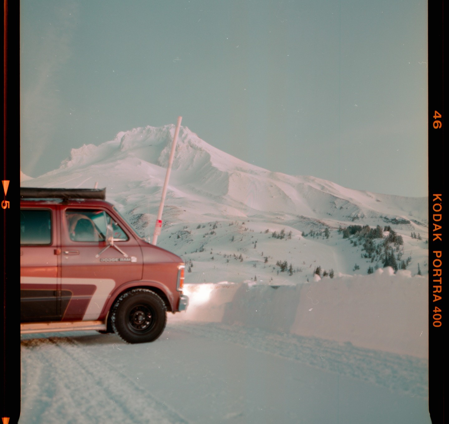 A red van is parked on a snowy road with a large snow-covered mountain in the background.