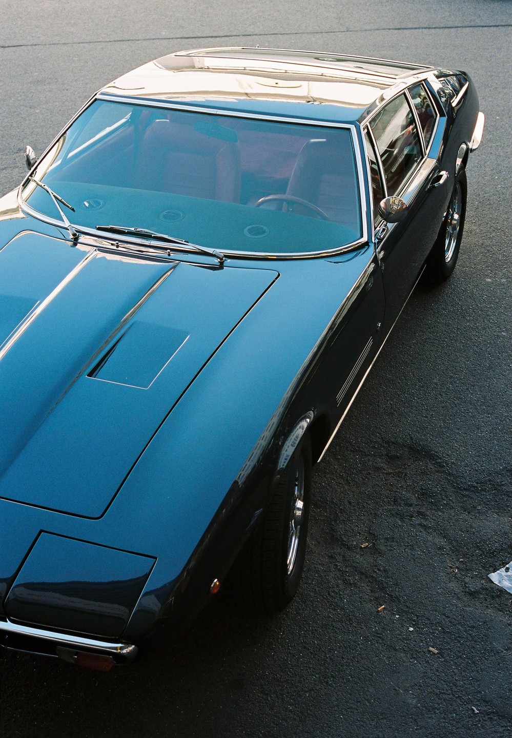 A dark blue vintage car is parked on an asphalt surface, viewed from above.