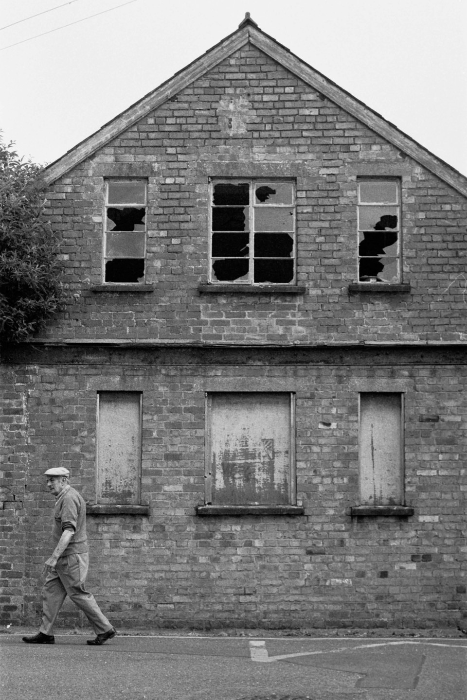 A man walks past a brick building with broken and boarded-up windows.