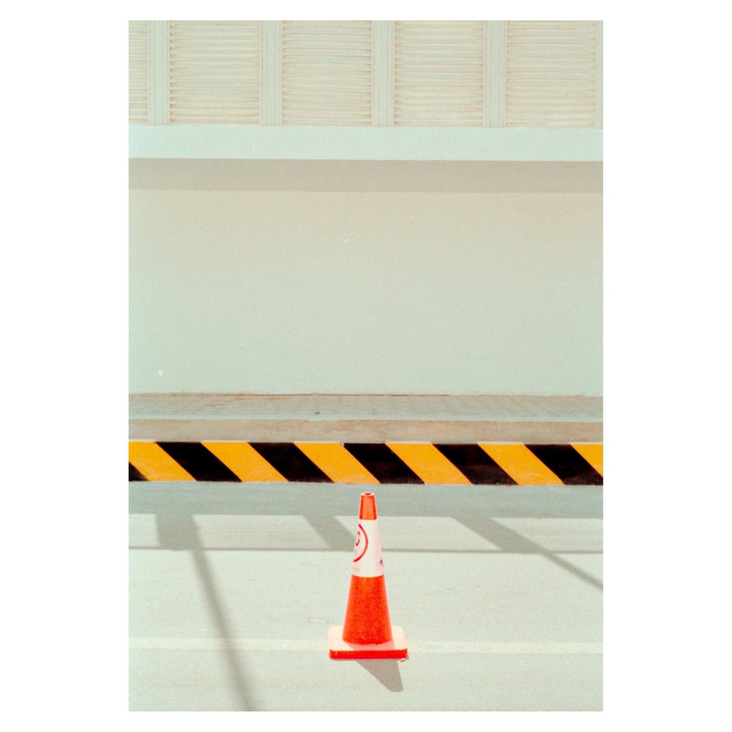 An orange traffic cone stands in front of a yellow and black striped barrier.