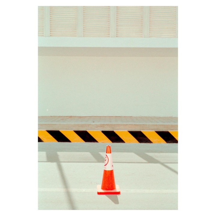 An orange traffic cone stands in front of a yellow and black striped barrier.