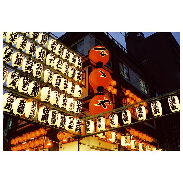 Many lanterns with Japanese writing hang from a building at night.