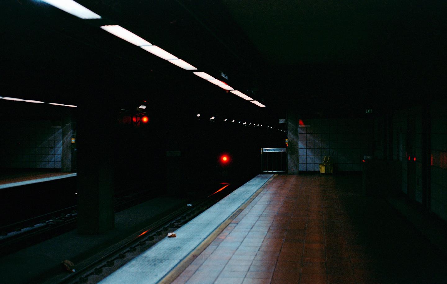 A dark subway platform is illuminated by overhead lights and red signals in the distance.