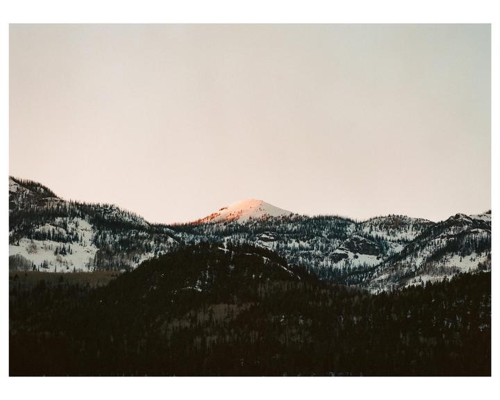 Snow-covered mountains are visible under a pale sky, with one peak illuminated by the setting sun.