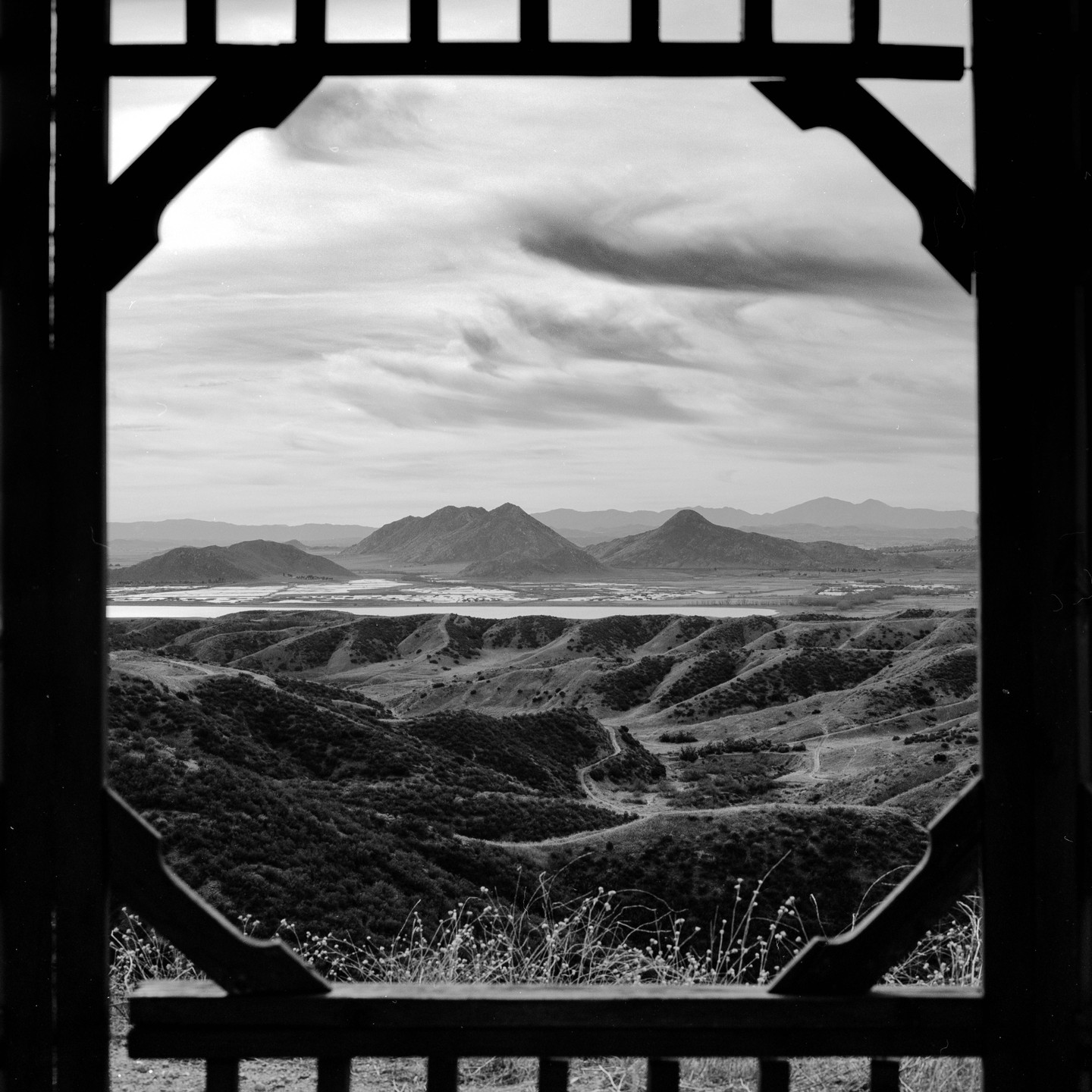 A black and white landscape shows rolling hills and mountains in the distance, framed by a dark wooden structure.