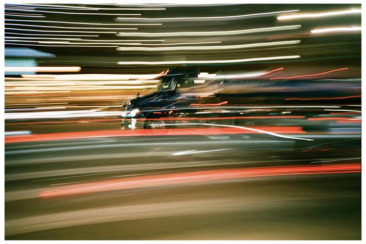 A vehicle is blurred by motion, surrounded by streaks of light from other vehicles and streetlights at night.