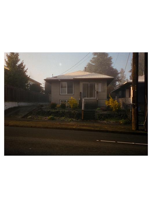 A house with a small front yard and steps leading to the entrance is seen from across the street.