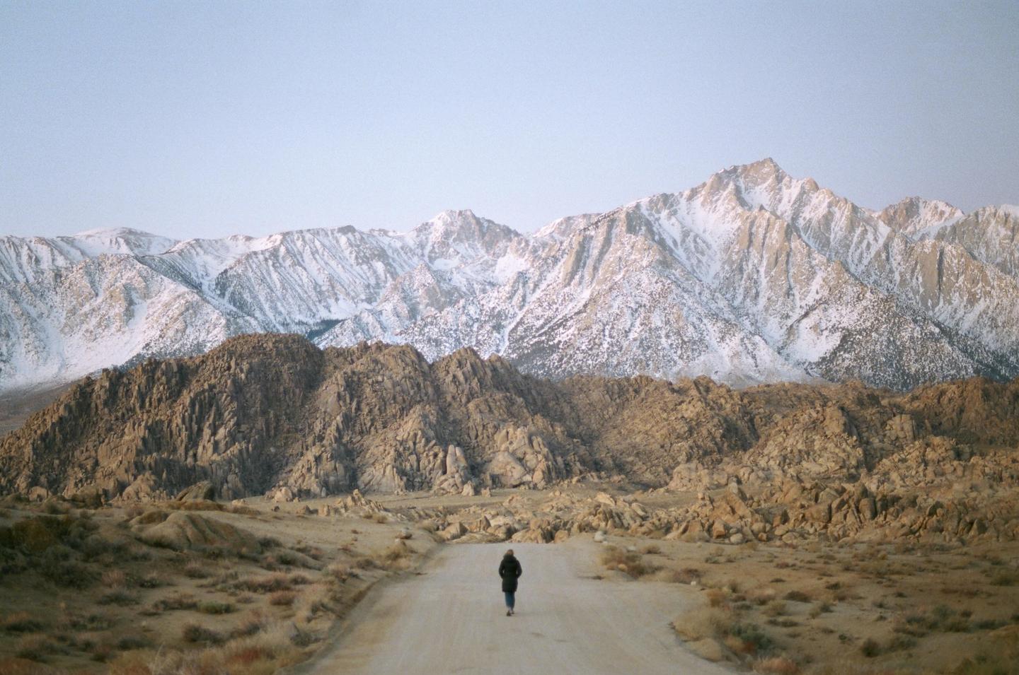 A person walks down a dirt road towards snow-capped mountains in Death Valley.