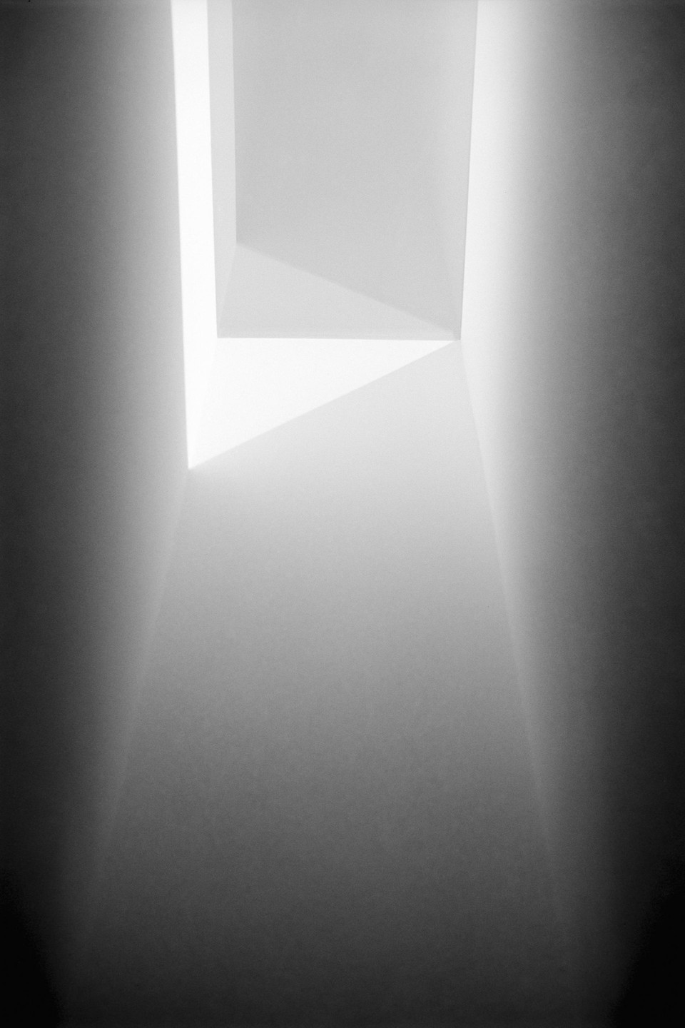 Light streams into a dark, narrow, abstract space from an opening above.