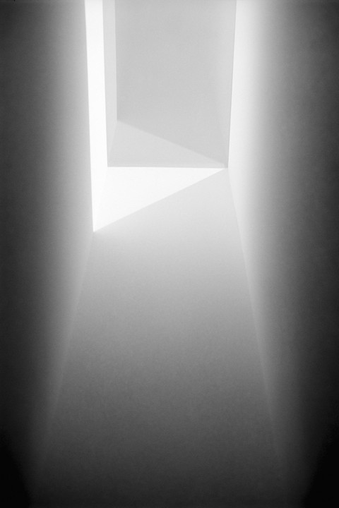 Light streams into a dark, narrow, abstract space from an opening above.