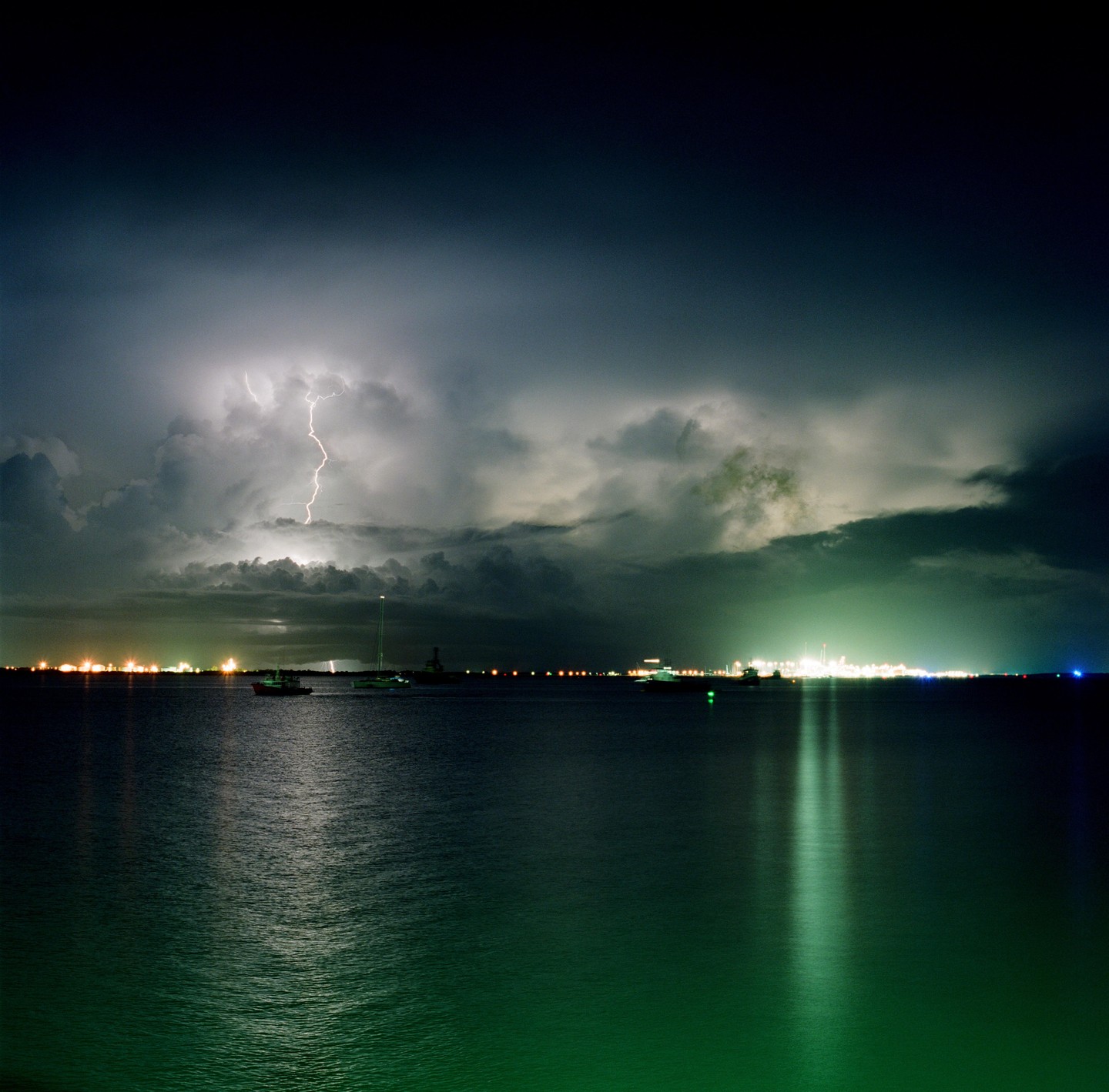 Lightning strikes over a body of water with city lights in the distance at night.