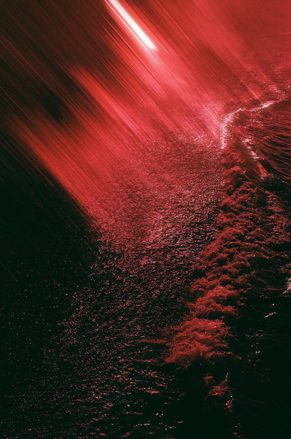 A red light streaks across a dark surface, illuminating a wave of water.