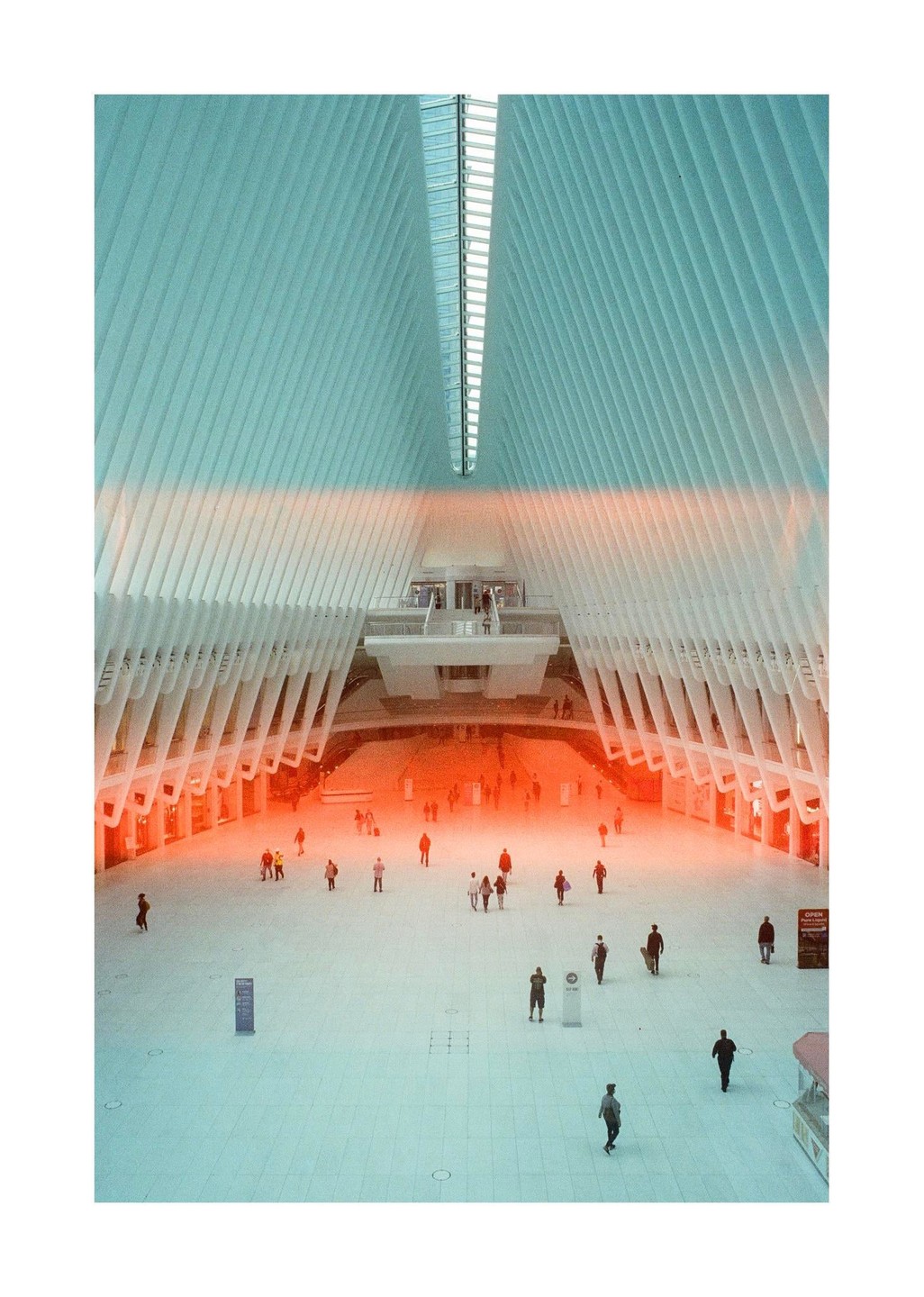 A large, modern, white building with a high ceiling and many people walking on the ground floor.