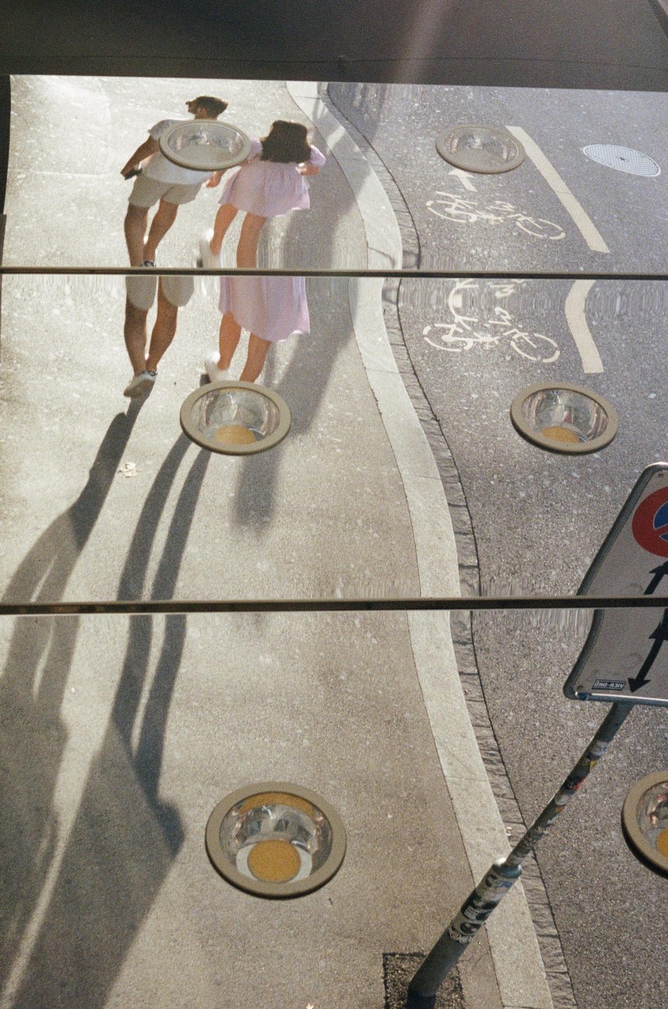 A man and a woman walk on a street with a bicycle lane, their reflections distorted by a wavy surface.