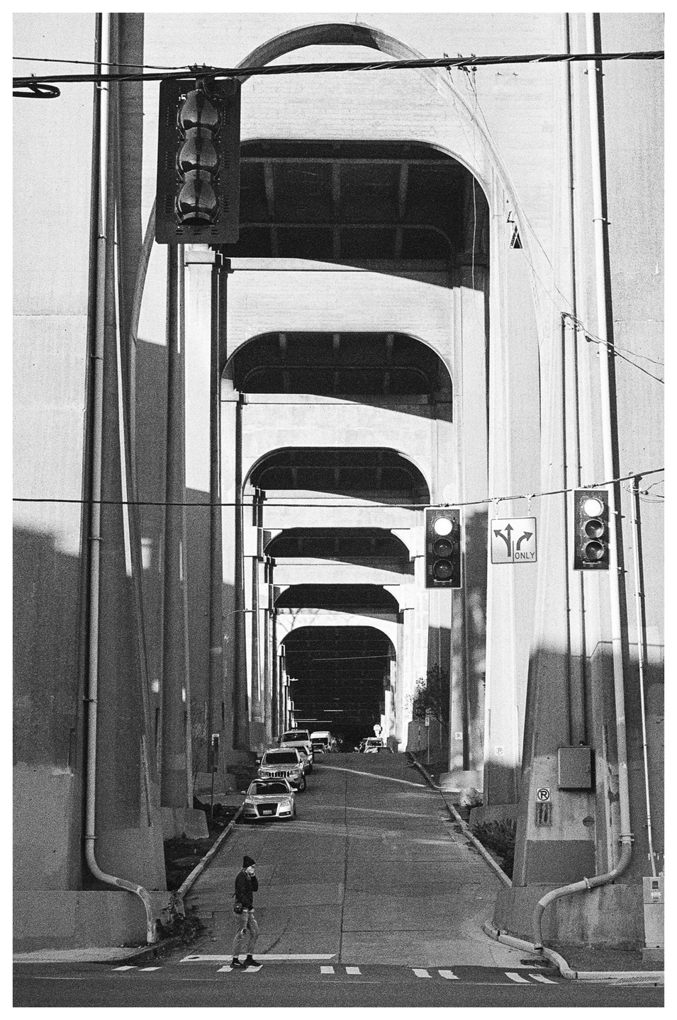 A person crosses a street under a bridge with multiple arches and traffic lights.