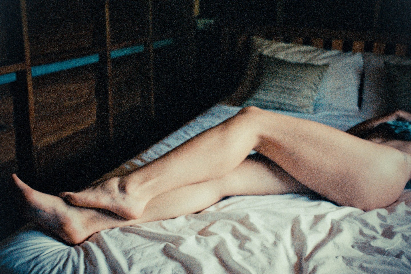 A woman's legs are visible as she lies on a bed with white sheets and a pillow.
