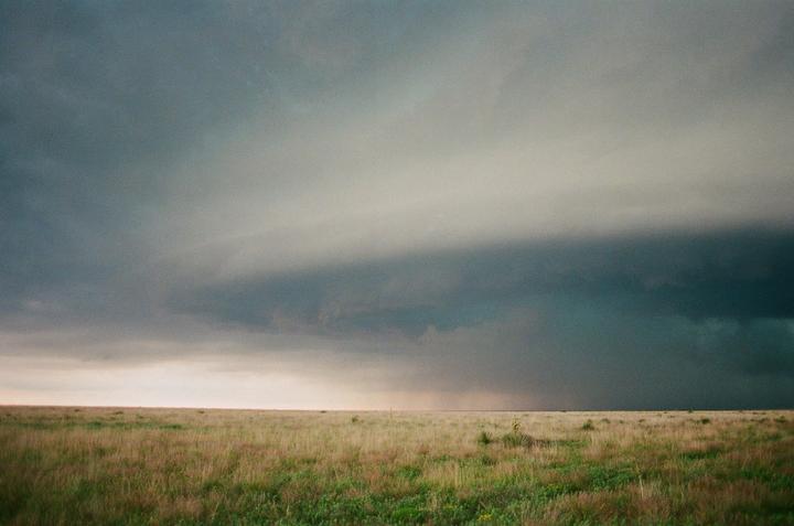 A vast field of grass stretches under a dramatic, dark storm sky.