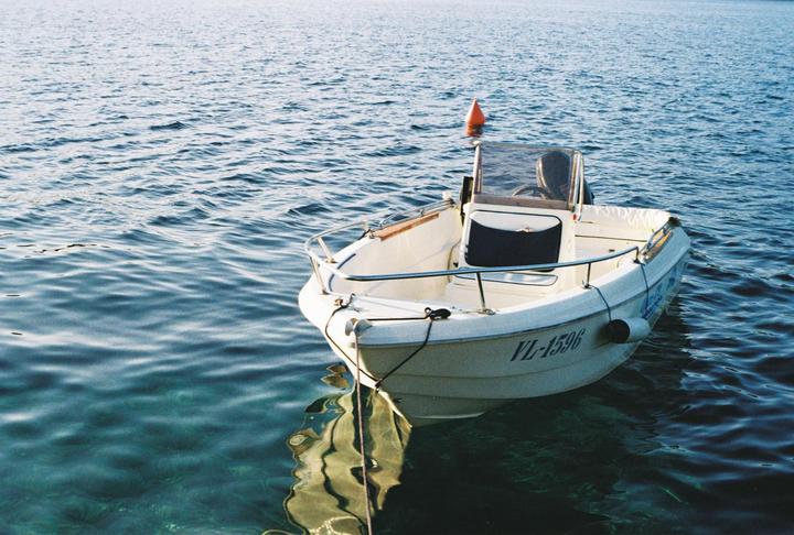 A small white motorboat is moored in clear blue water with an orange buoy visible in the background.