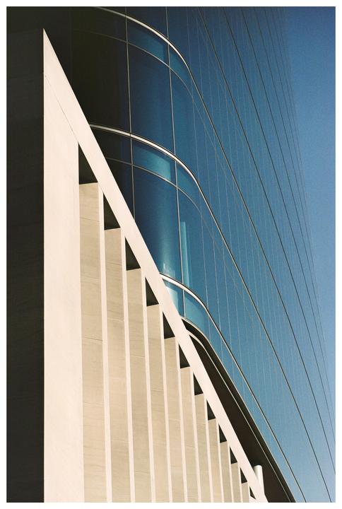 A modern building with a blue glass facade and a white concrete side is shown from a low angle.