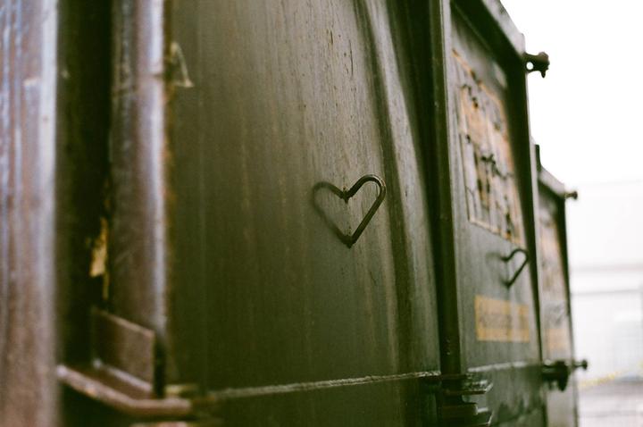 A heart shape is carved into the side of a dark, weathered dumpster.
