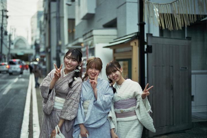 Three women in kimonos pose for a photo on a city street.