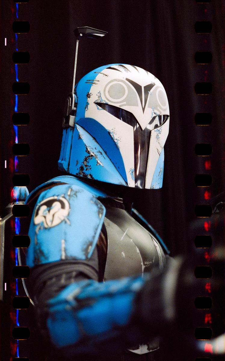 A person in a blue and white helmet and armor is visible in a close-up shot.