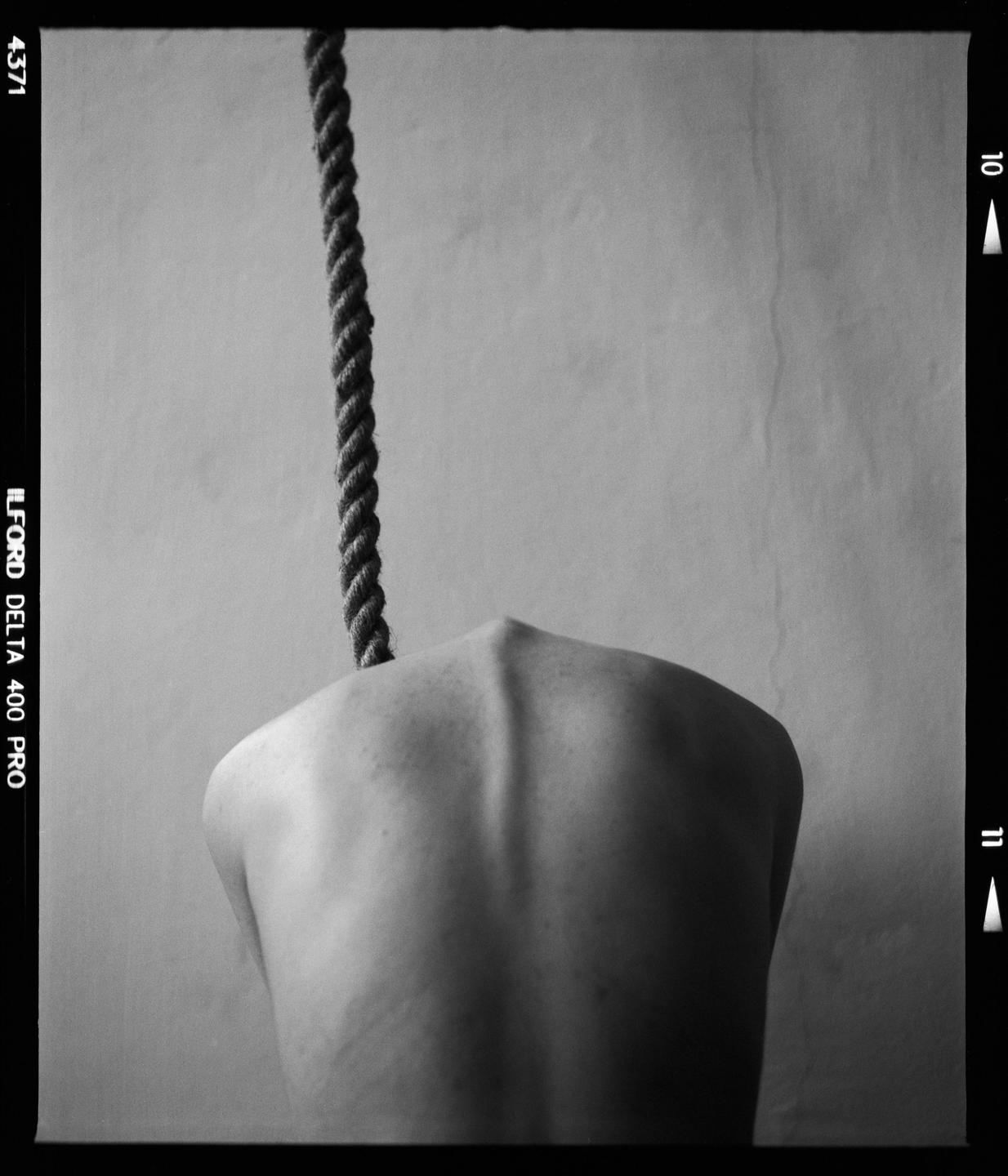 A person's bare back is visible with a rope hanging down behind them.