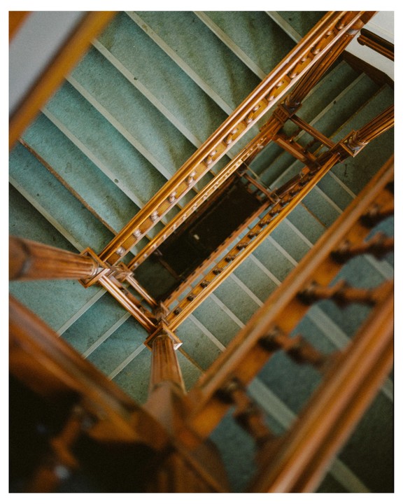 A view looking down a wooden staircase with green carpeted steps.
