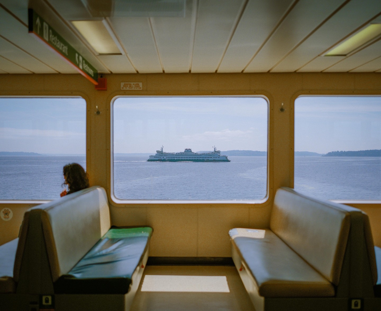 A woman sits on a ferry looking out at another ferry on the water.