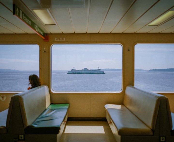 A woman sits on a ferry looking out at another ferry on the water.