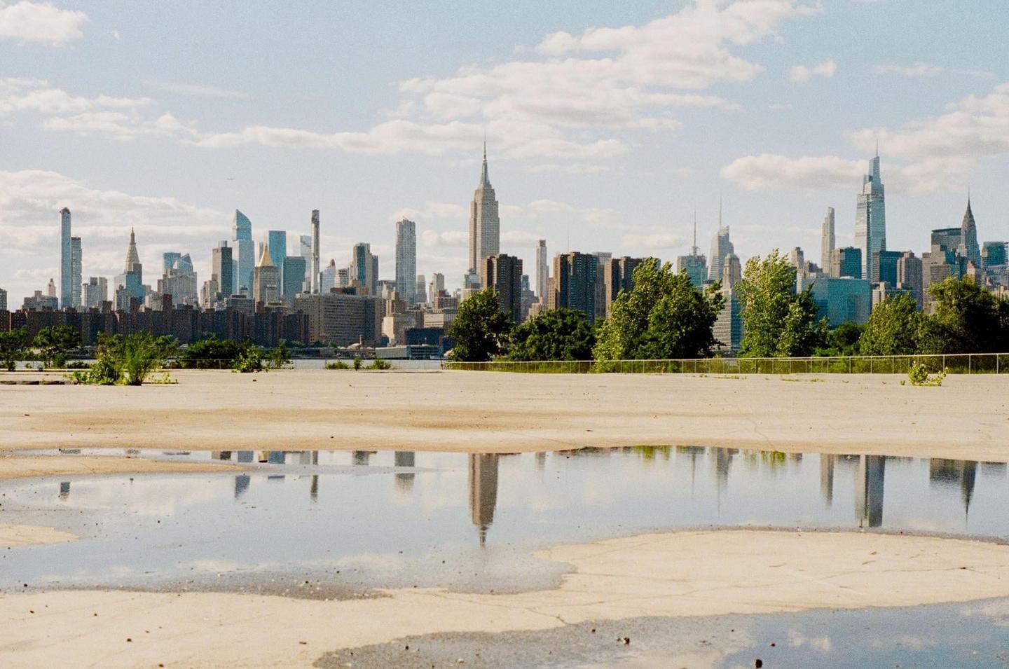 A cityscape with tall buildings is reflected in a puddle on a concrete surface.