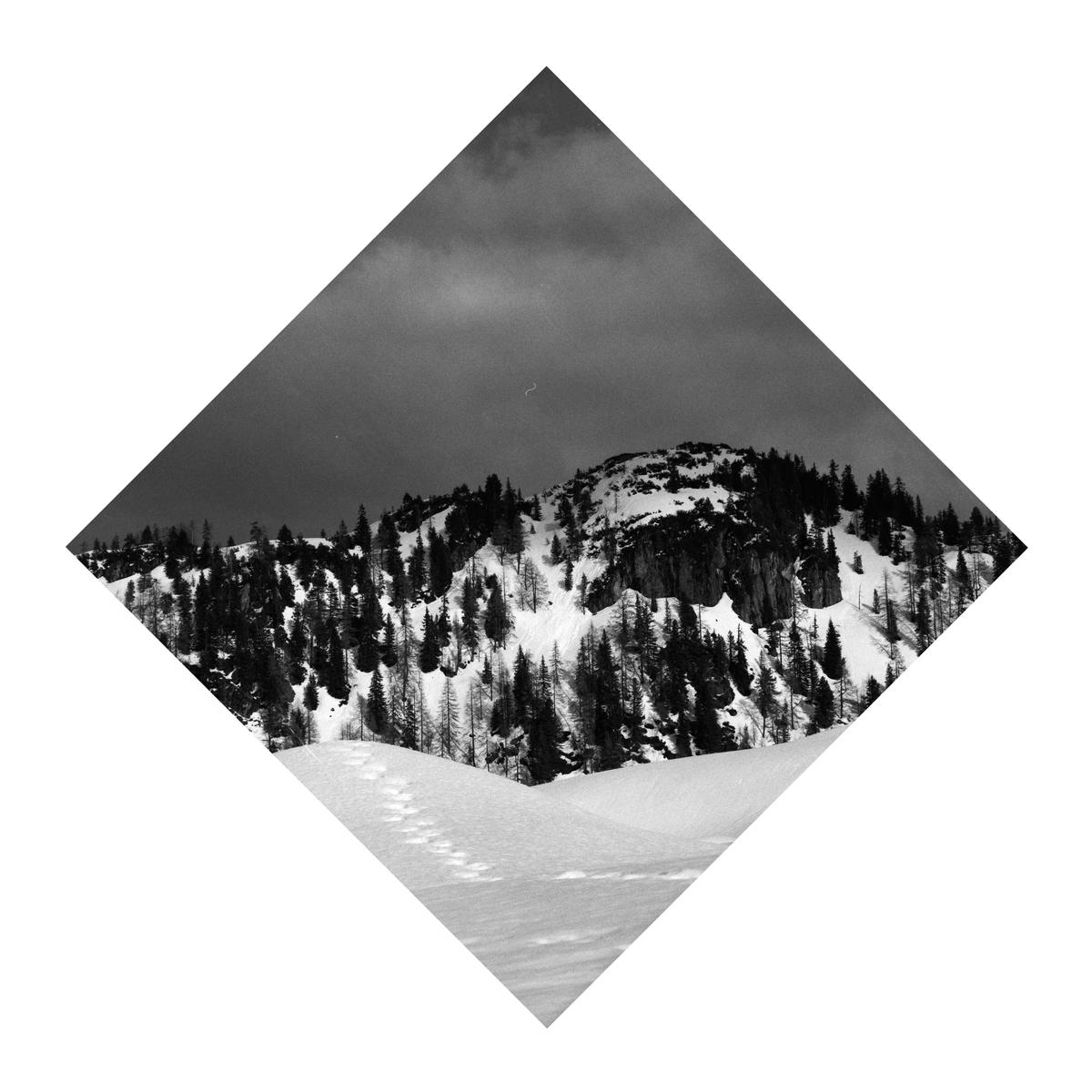 A snow-covered mountain with trees under a cloudy sky is framed in a diamond shape.