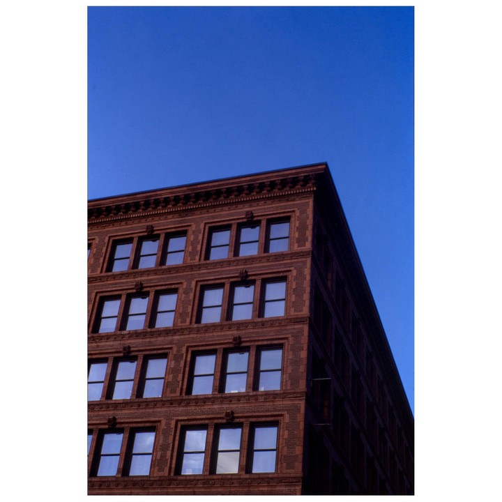 A red brick building with many windows stands against a clear blue sky.