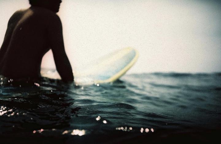 A surfer sits on a surfboard in the ocean, with the water rippling around them.