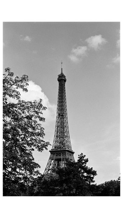 The Eiffel Tower rises above trees and clouds.