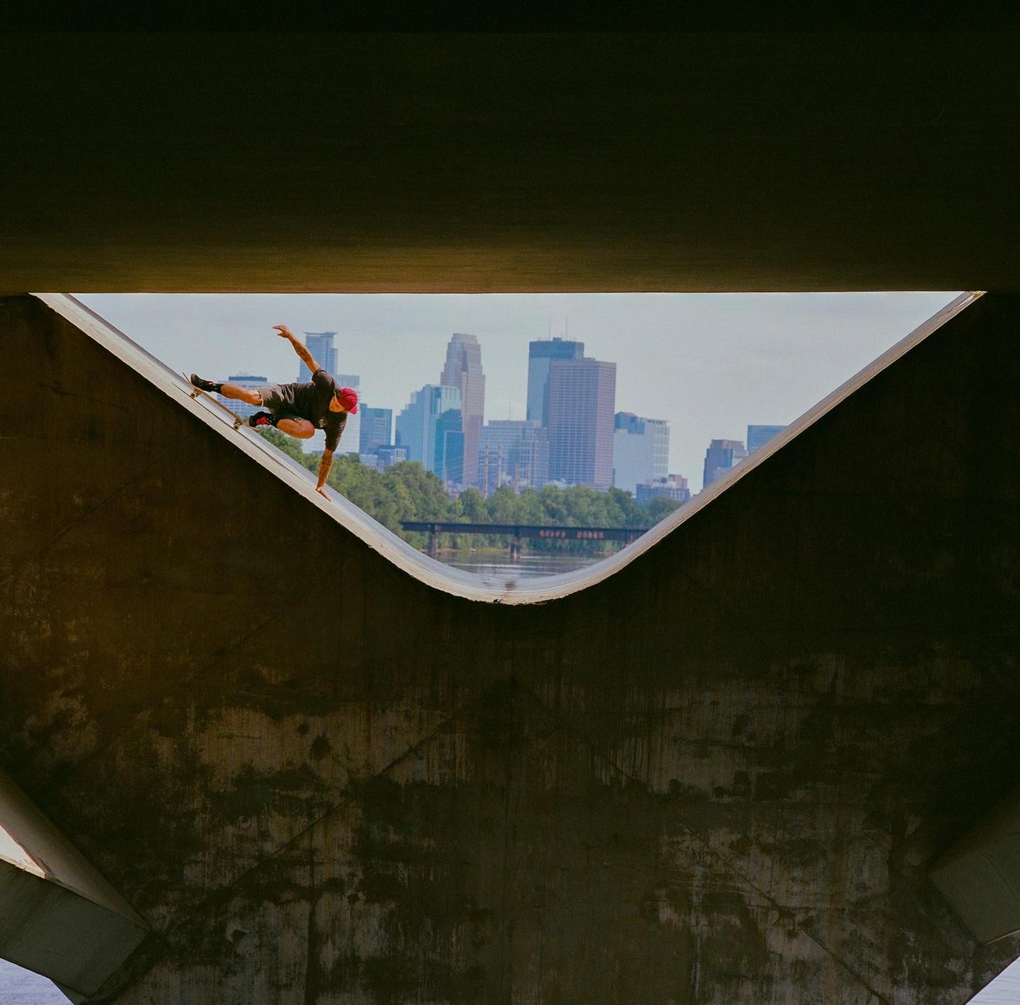 A skateboarder balances on a concrete ramp with a city skyline in the background.