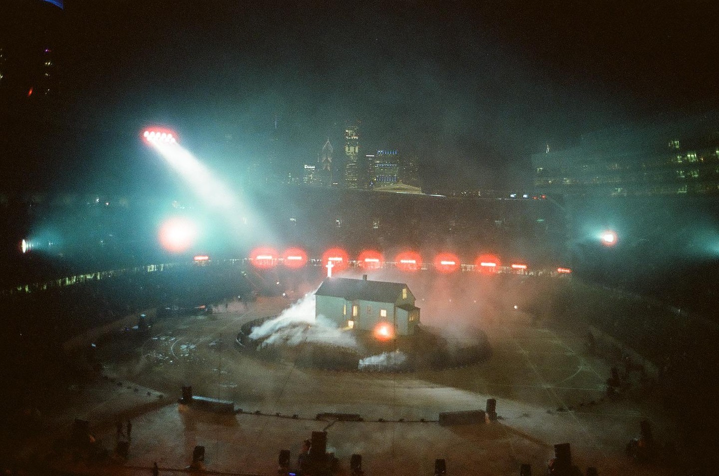 A small house sits on a stage in a stadium at night, surrounded by smoke and bright lights.