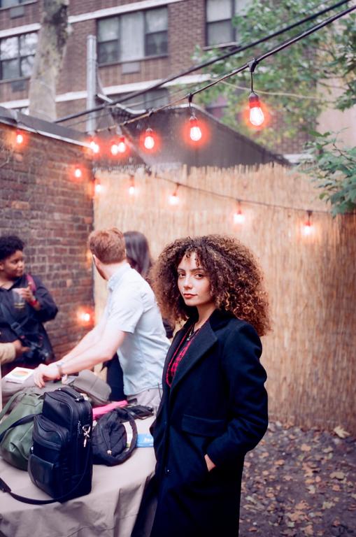 A woman with curly hair stands in a backyard with string lights and other people.