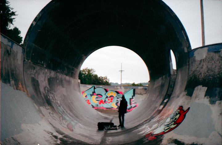 A person stands in a concrete skate park tunnel with graffiti on the walls.