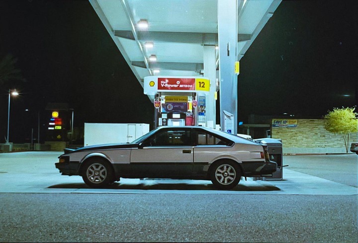 A two-tone car is parked at a gas station at night.